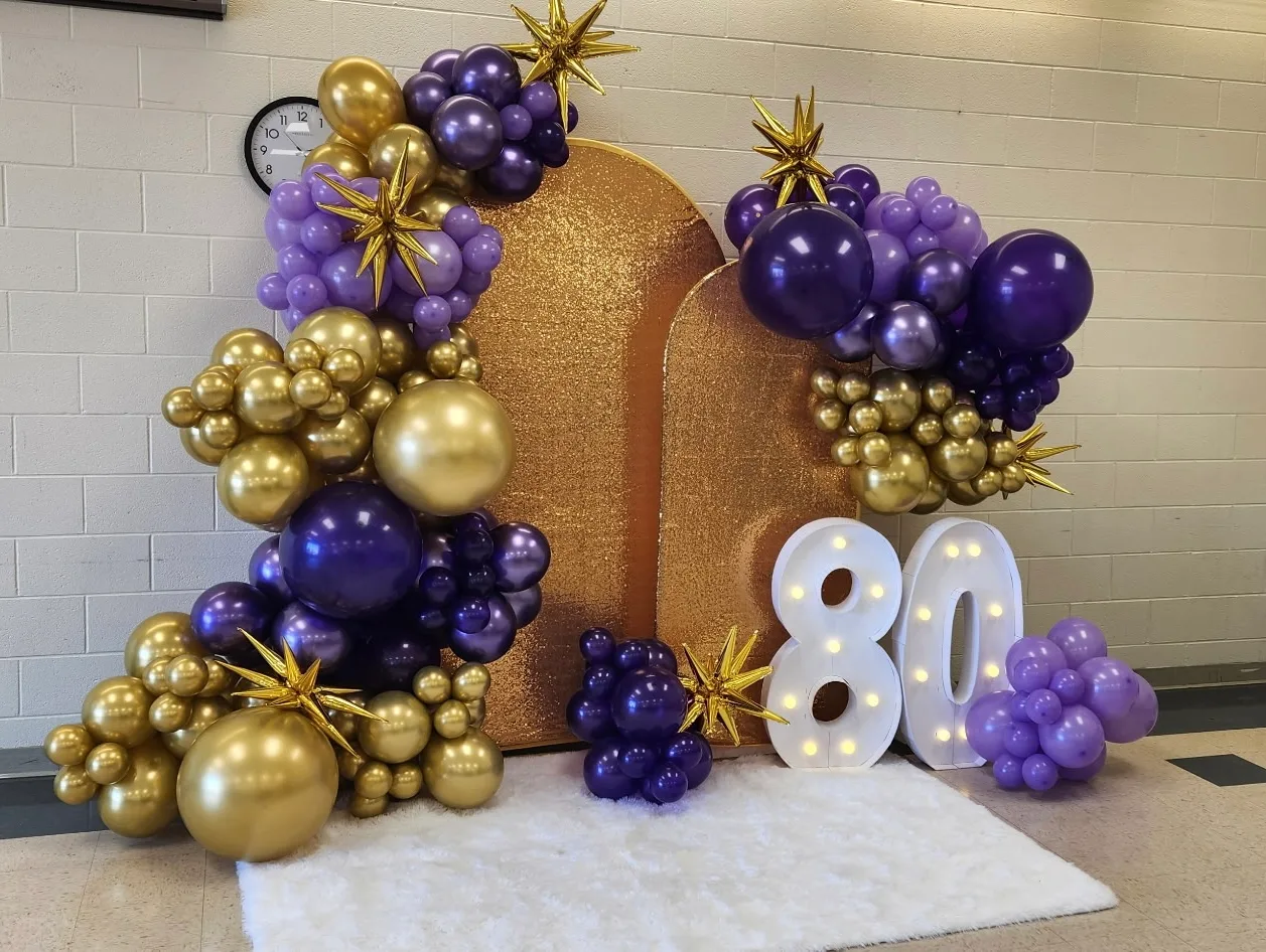80th birthday display with gold and purple balloon garlands and marquee 80 numbers.