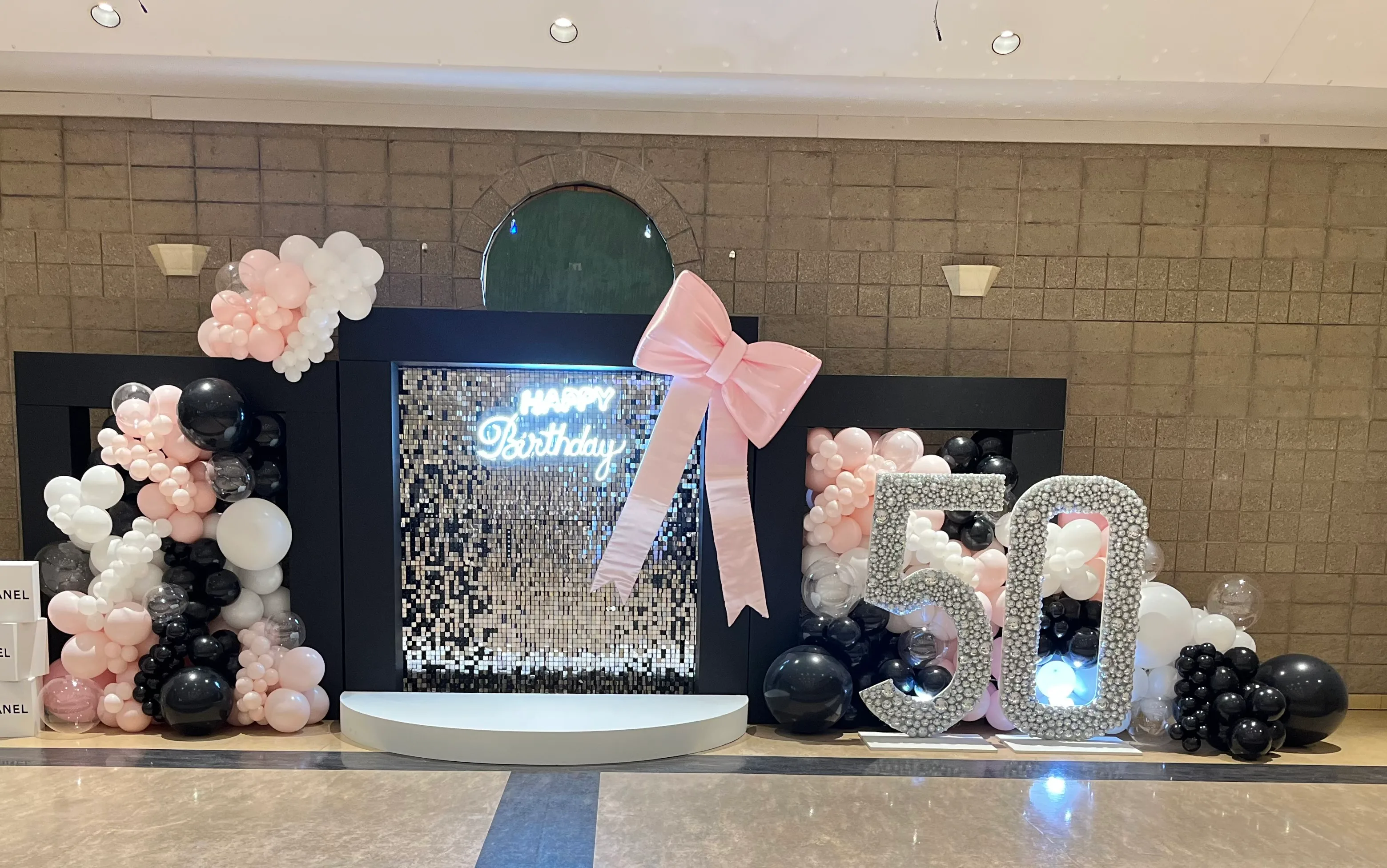50th birthday backdrop with a pink bow, sequin wall, and marquee 50 numbers.